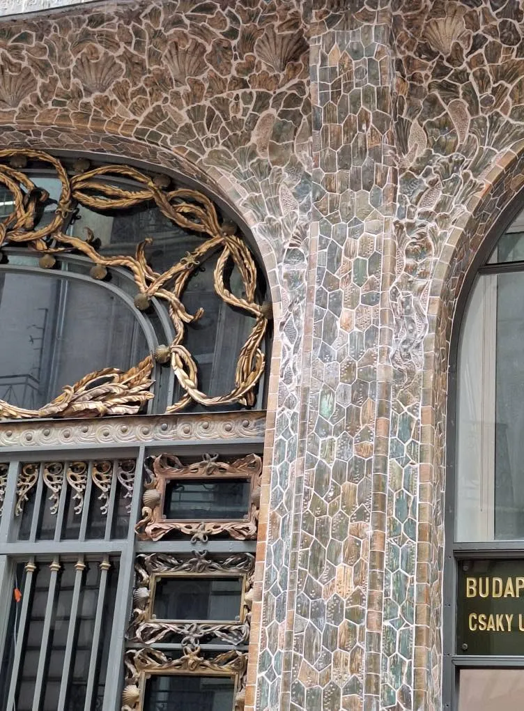 Détail de la façade : carreaux de céramique à décor de coquilles, au-dessus d'une grille en ferronnerie dorée.