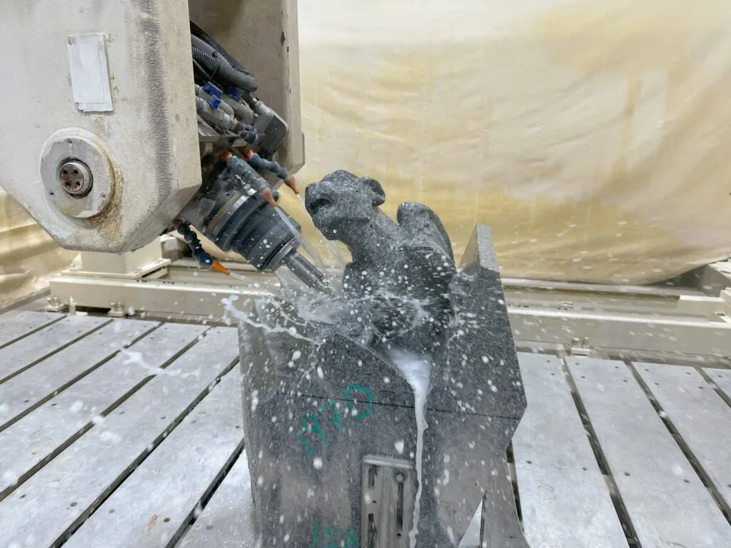 Un centre d'usinage taille une chimère en pierre ; l'eau d'arrosage jaillit autour de l'outil.